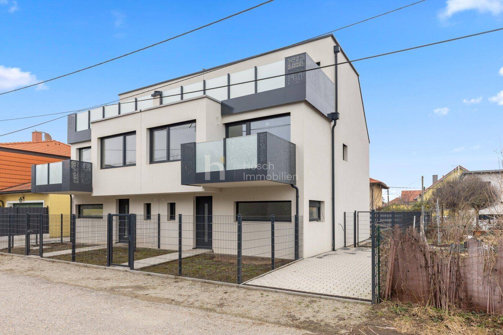 Moderne Mehrfamilienhausfassade mit Balkonen und klaren Linien unter blauem Himmel.