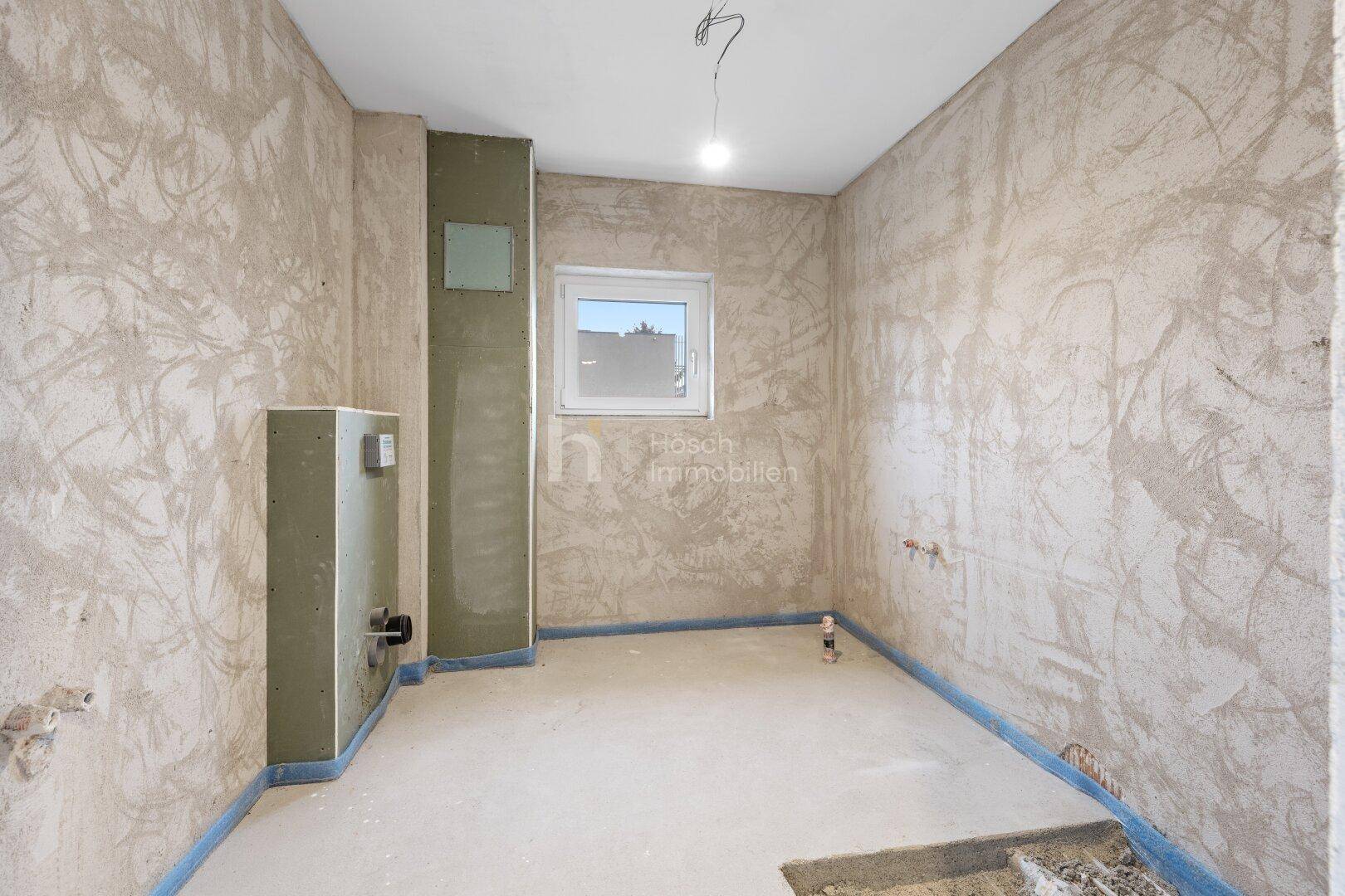 Unfertiges Badezimmer mit Fenster und vorbereiteten Anschlüssen.