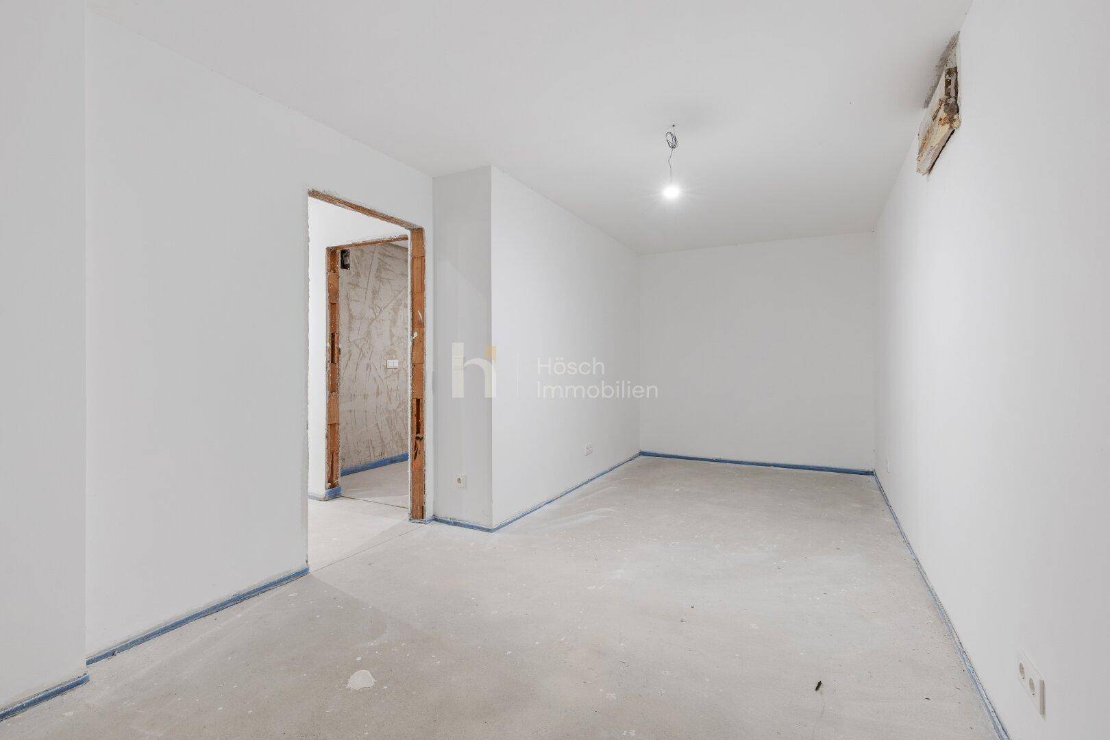 Leerer Raum im Rohbau mit weiß gestrichenen Wänden und Türöffnung, wartet auf Fertigstellung.