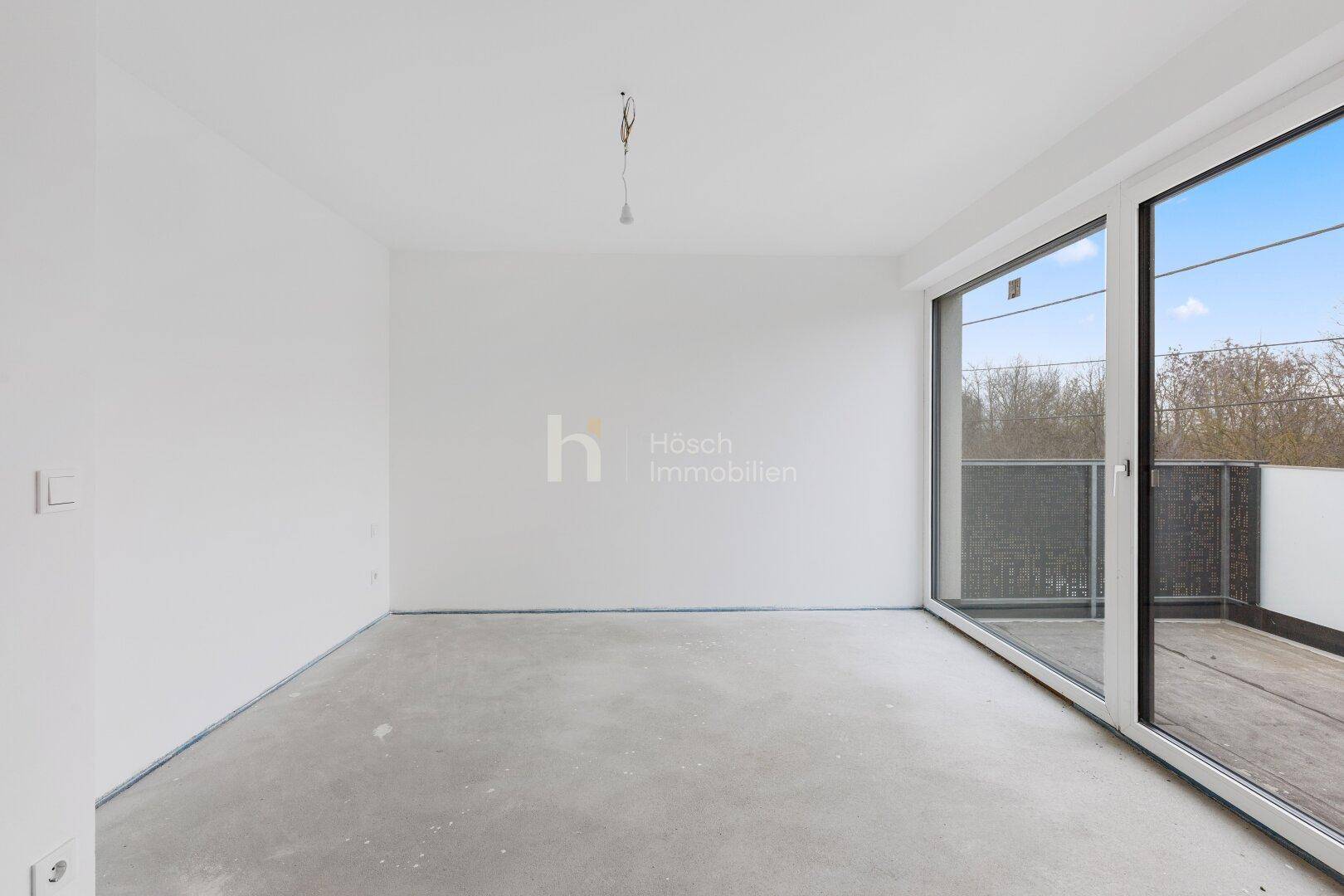 Unmöbliertes Schlafzimmer mit großen Fenstern und Zugang zu einem Balkon.