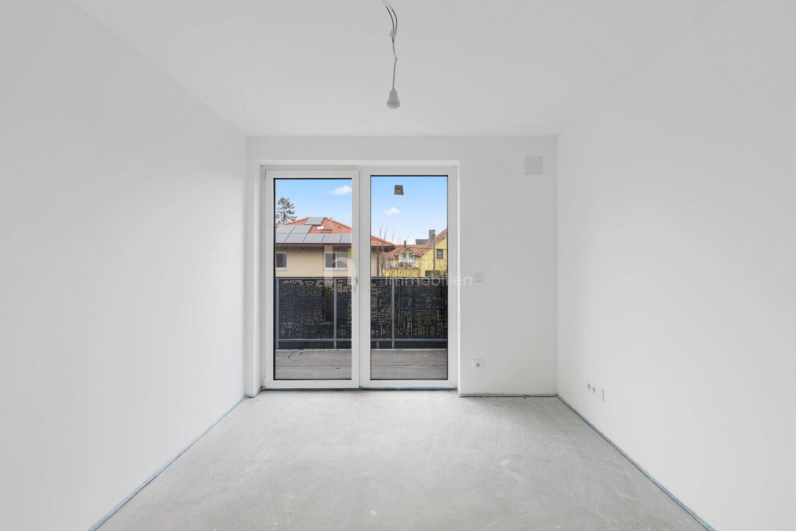 Unmöbliertes Schlafzimmer mit großen Fenstern und Zugang zu einem Balkon.