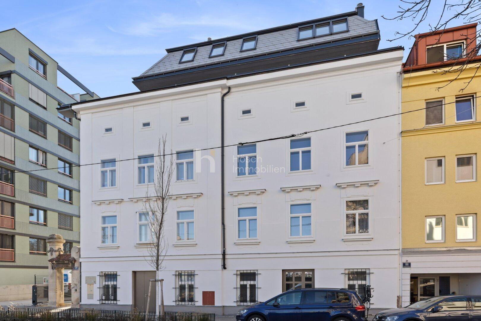 Vorderansicht eines sanierten Gebäudes mit Mansarddach und vielen Fenstern in der Stadt.