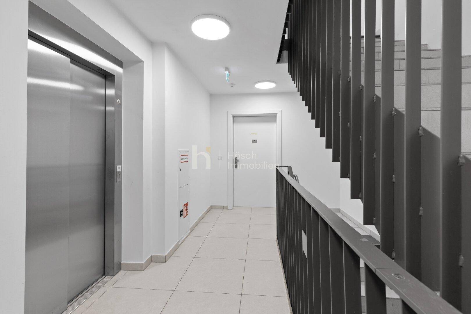 Heller Flur mit Aufzug, Treppenhaus und modernen Deckenleuchten in einem Mehrfamilienhaus.