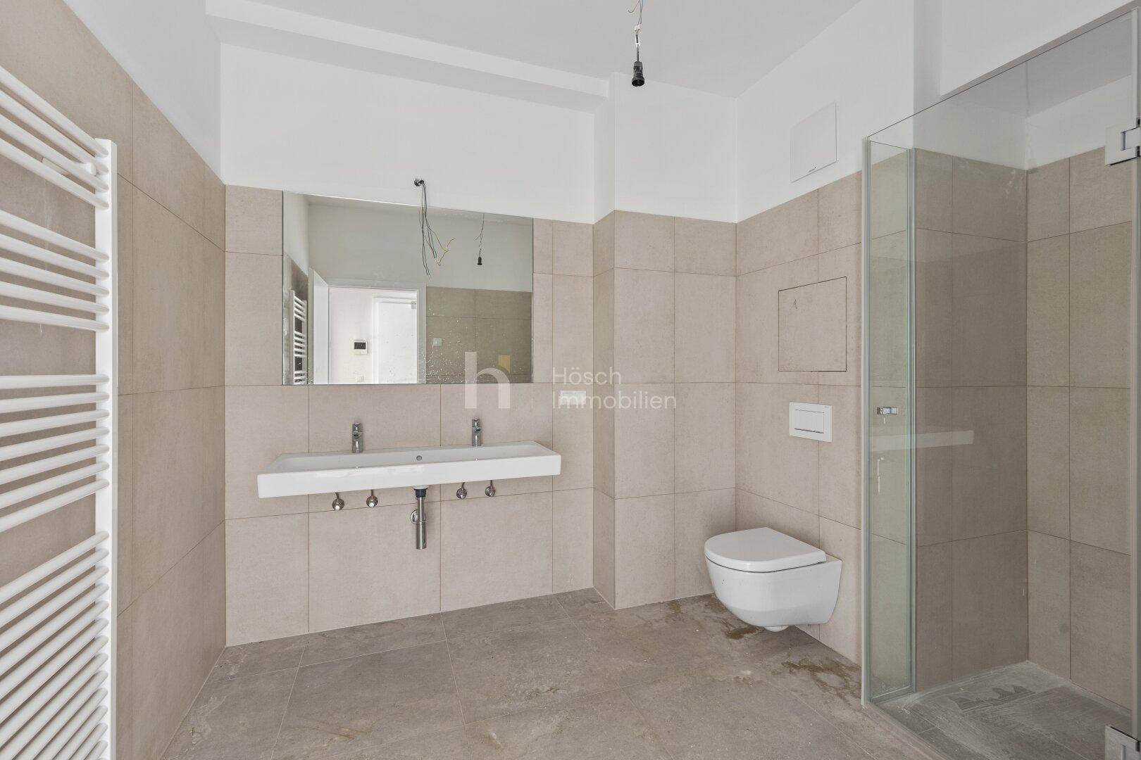 Modernes Badezimmer mit Doppelwaschbecken, wandhängendem WC und ebenerdiger Glasdusche.