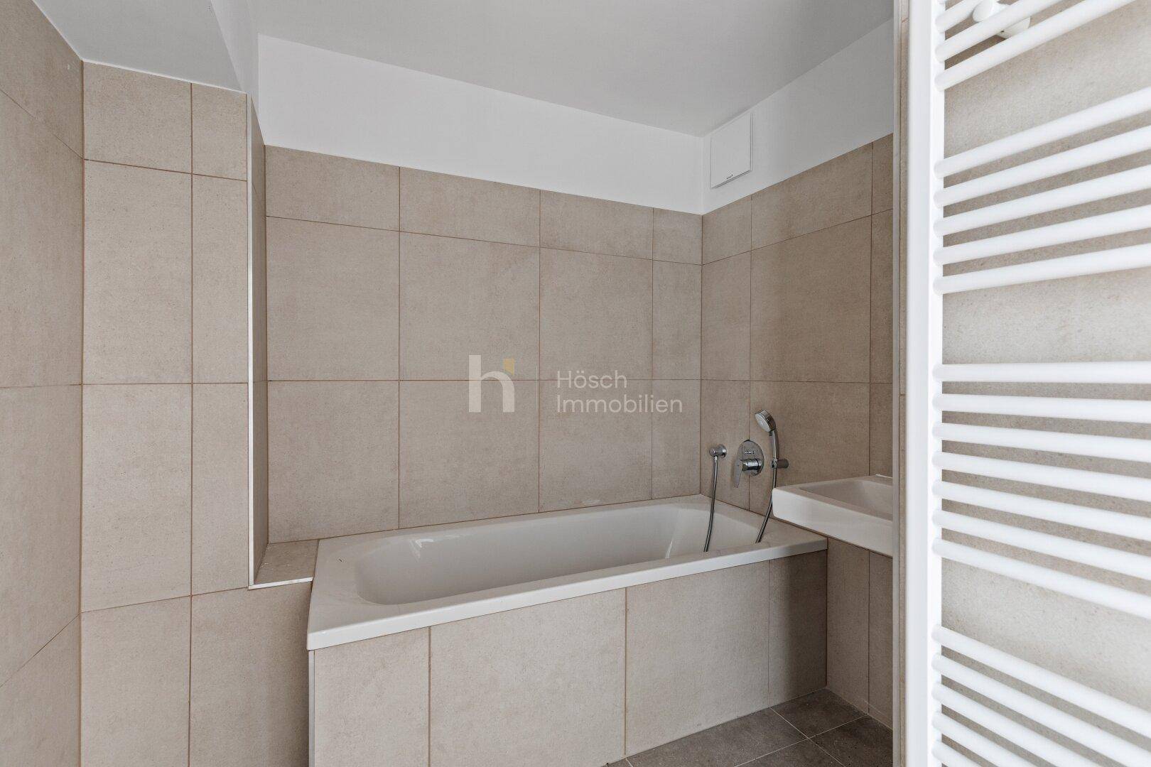 Modernes Badezimmer mit beigefarbenen Fliesen, Badewanne und beheiztem Handtuchhalter.