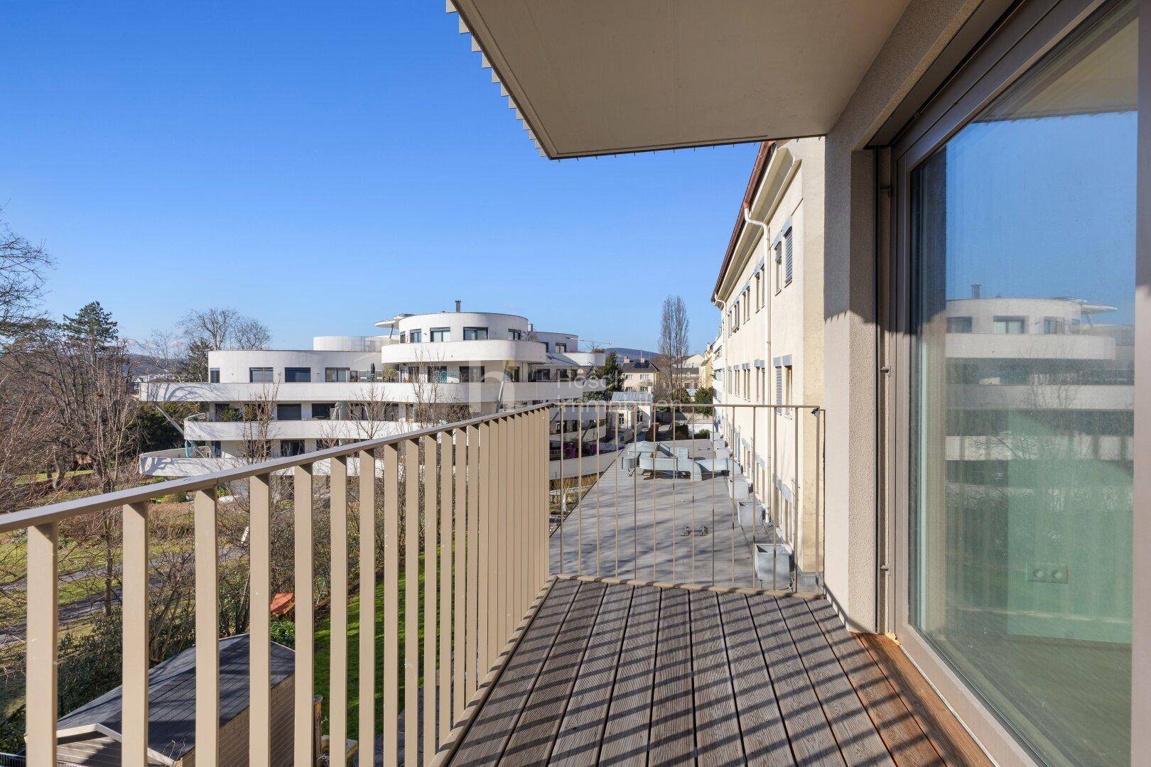 Geräumiger Balkon mit Holzboden und Blick auf moderne Wohngebäude und die Umgebung.