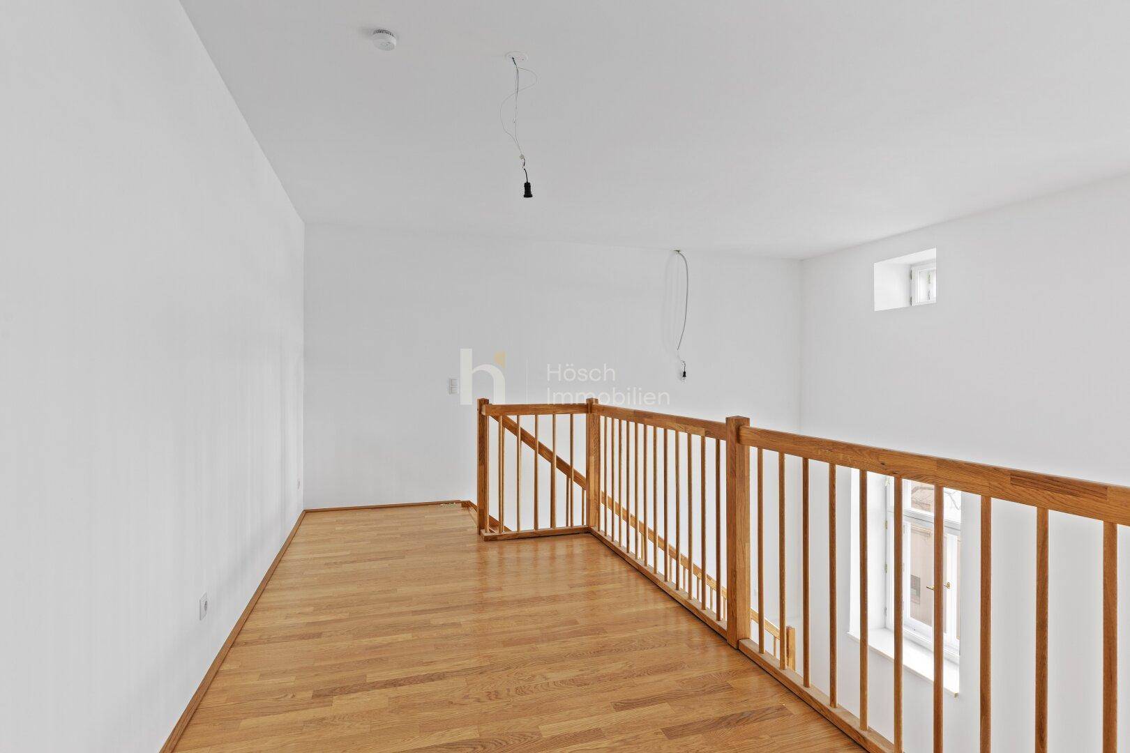 Heller Raum mit Holzboden und Holzgeländer, möglicherweise eine Galerie oder ein offener Flurbereich.