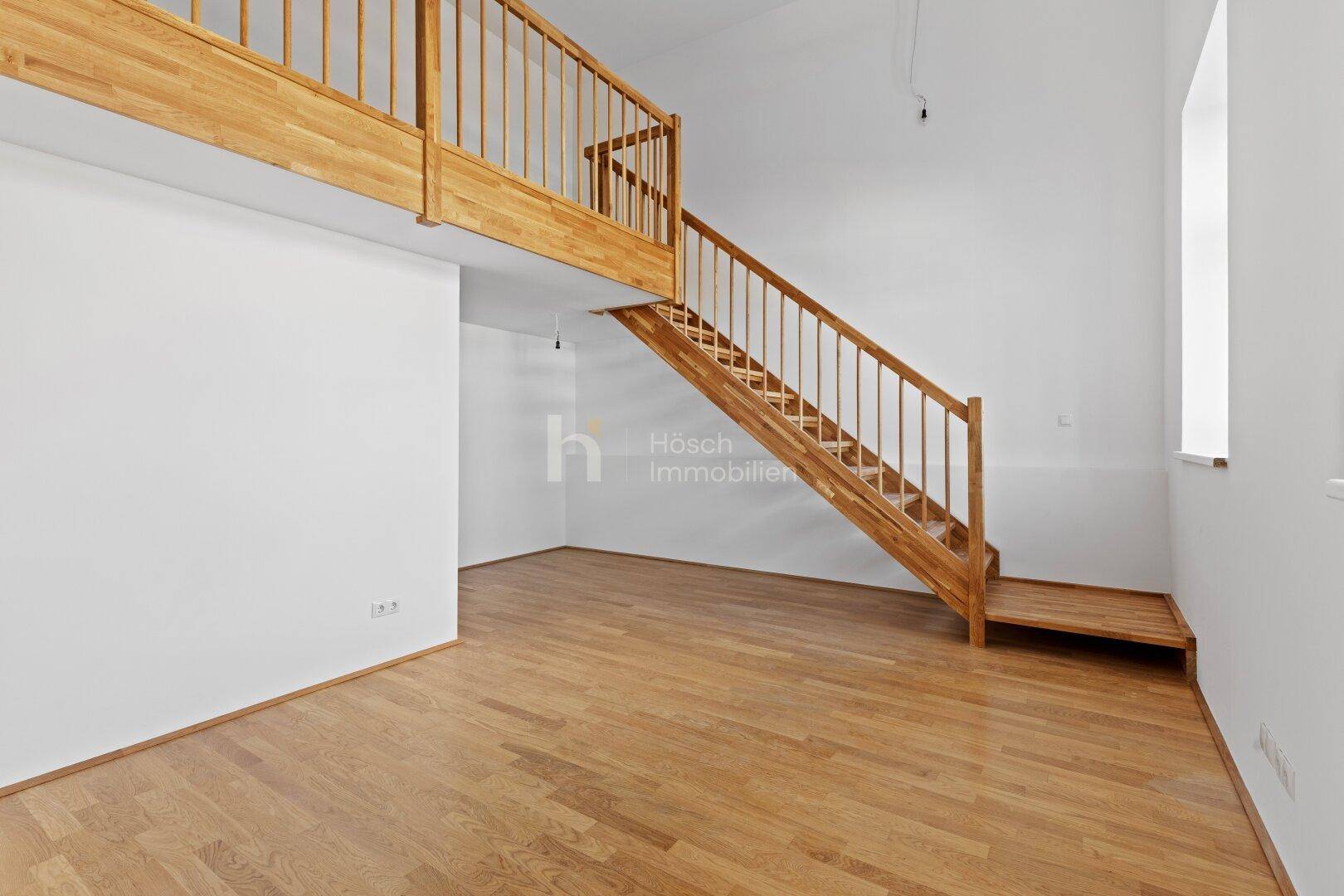 Hoher Wohnraum mit Holztreppe, die zu einer Galerie oder einem oberen Bereich führt.