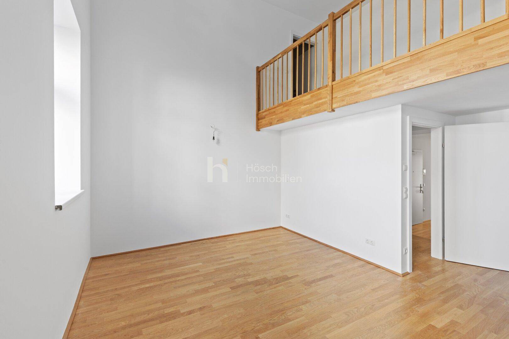 Hoher Wohnbereich mit Holzgalerie und hellem Parkettboden, der viel Raum bietet.
