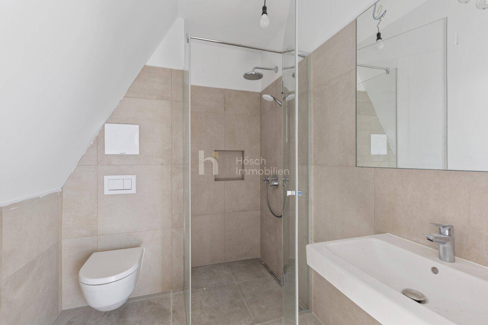 Modernes Badezimmer mit begehbarer Dusche, Wand-WC und Waschbecken unter Dachschräge.