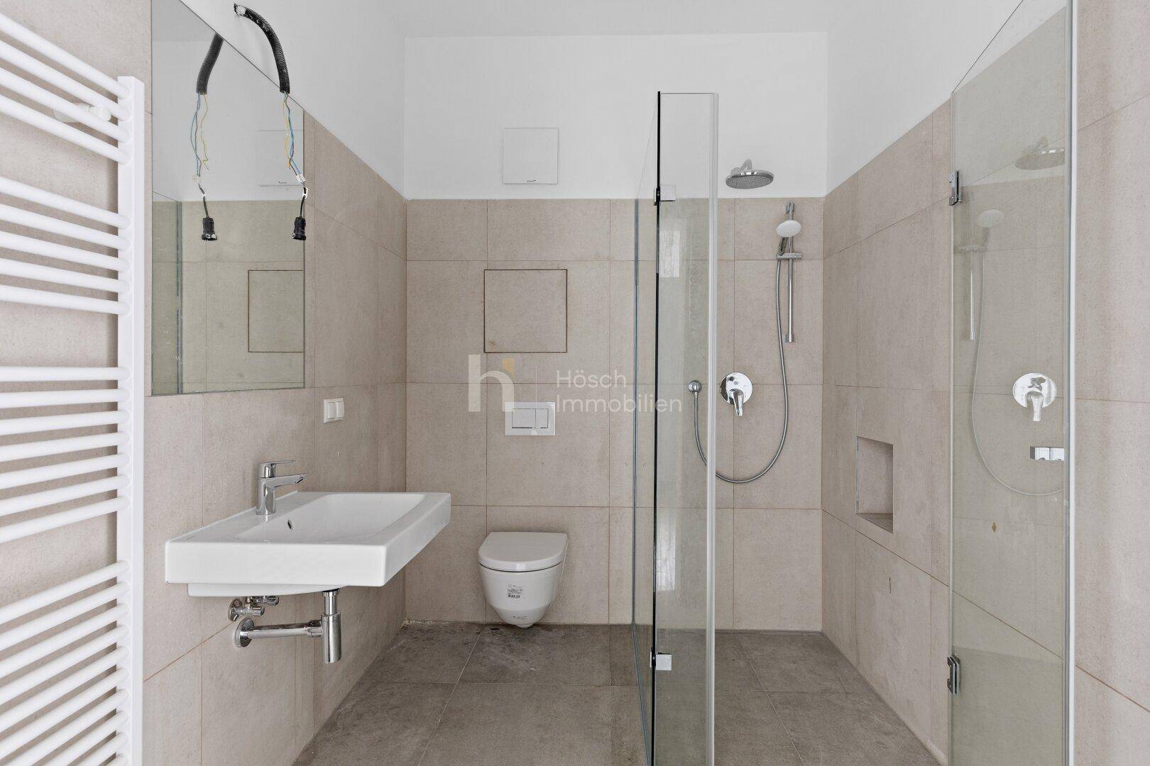 Modernes Badezimmer mit beigefarbenen Fliesen, ebenerdiger Dusche und wandhängendem WC.