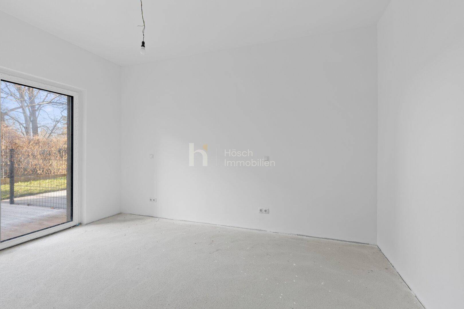 Heller, unmöblierter Raum mit Betonboden und großer Glastür, die viel Tageslicht hereinlässt.