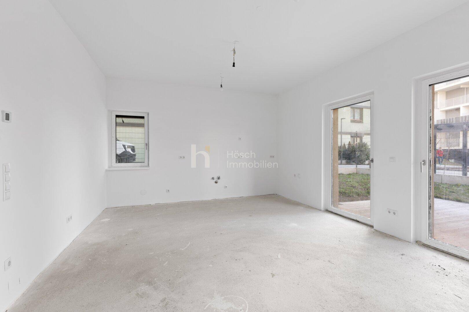 Heller, unmöblierter Raum mit Betonboden, weißen Wänden und großem Fenster sowie Terrassenzugang.