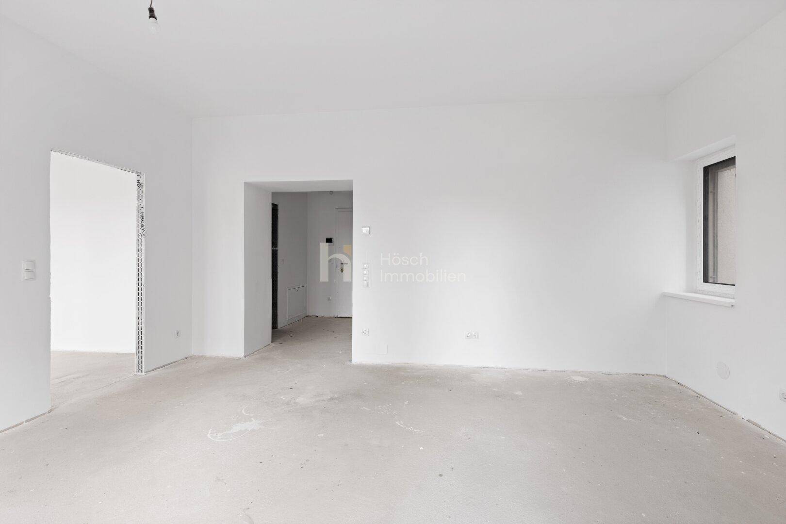Heller, unmöblierter Wohnraum mit weißen Wänden und Betonboden, bereit für den Erstbezug.