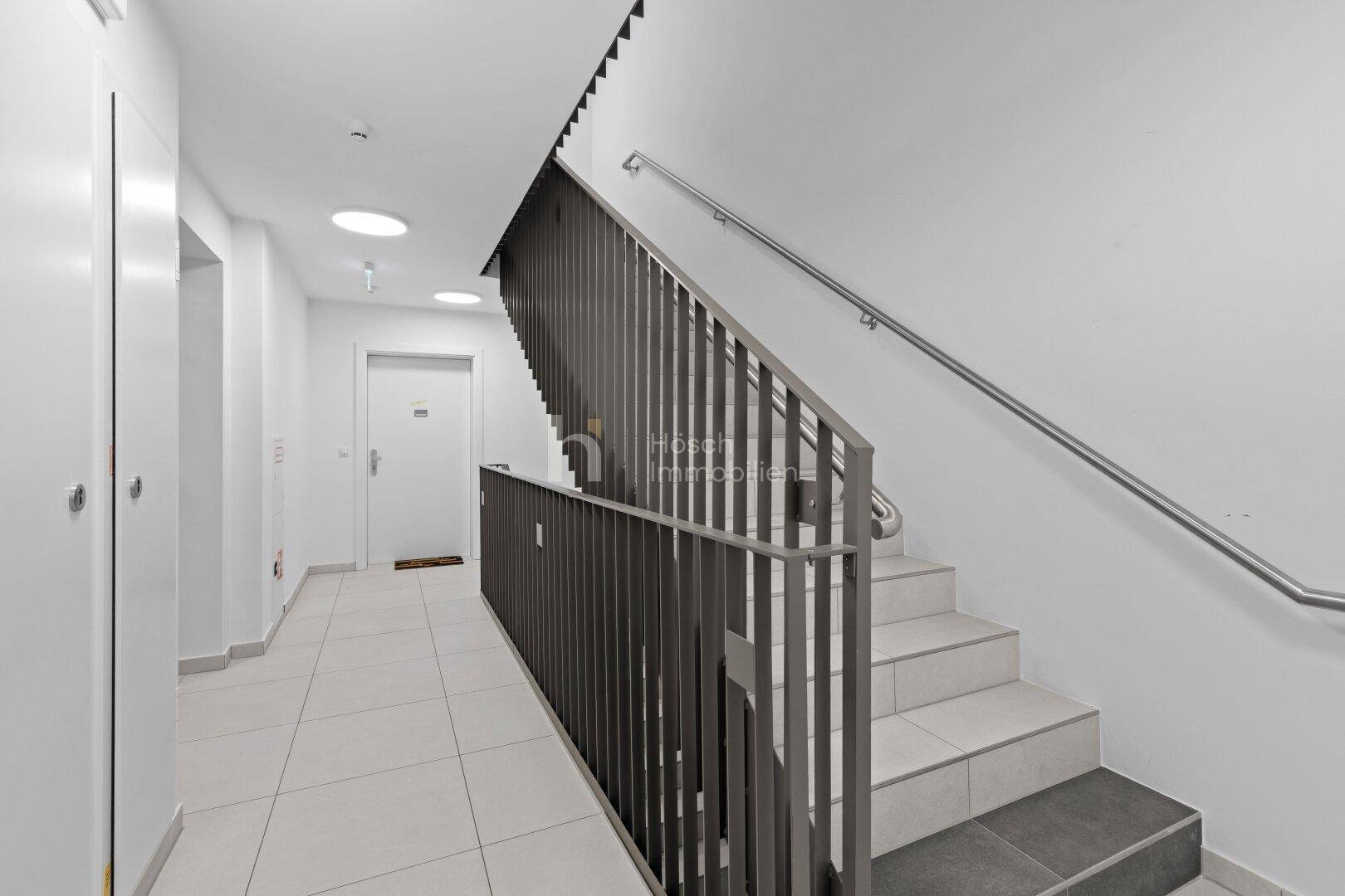 Modernes Treppenhaus mit Metallgeländer und Fliesenboden in einem Mehrfamilienhaus.