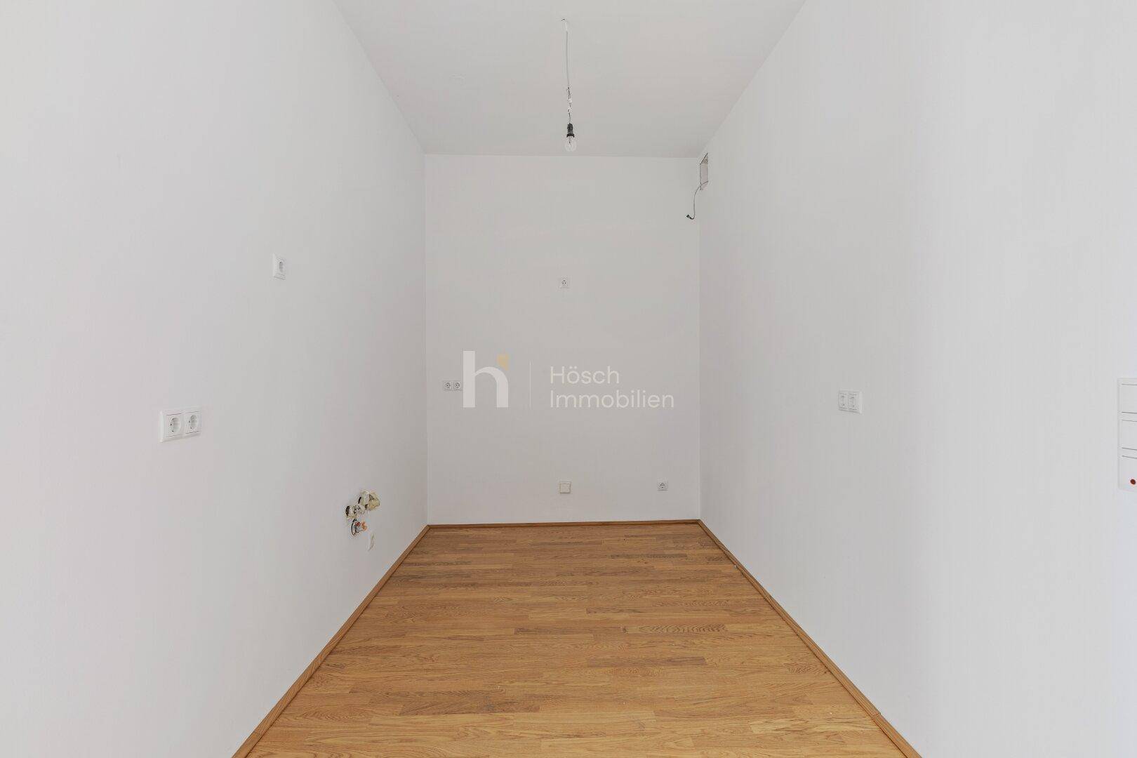 Leerer Raum mit Holzboden und Küchenanschlüssen, ideal für die individuelle Gestaltung.