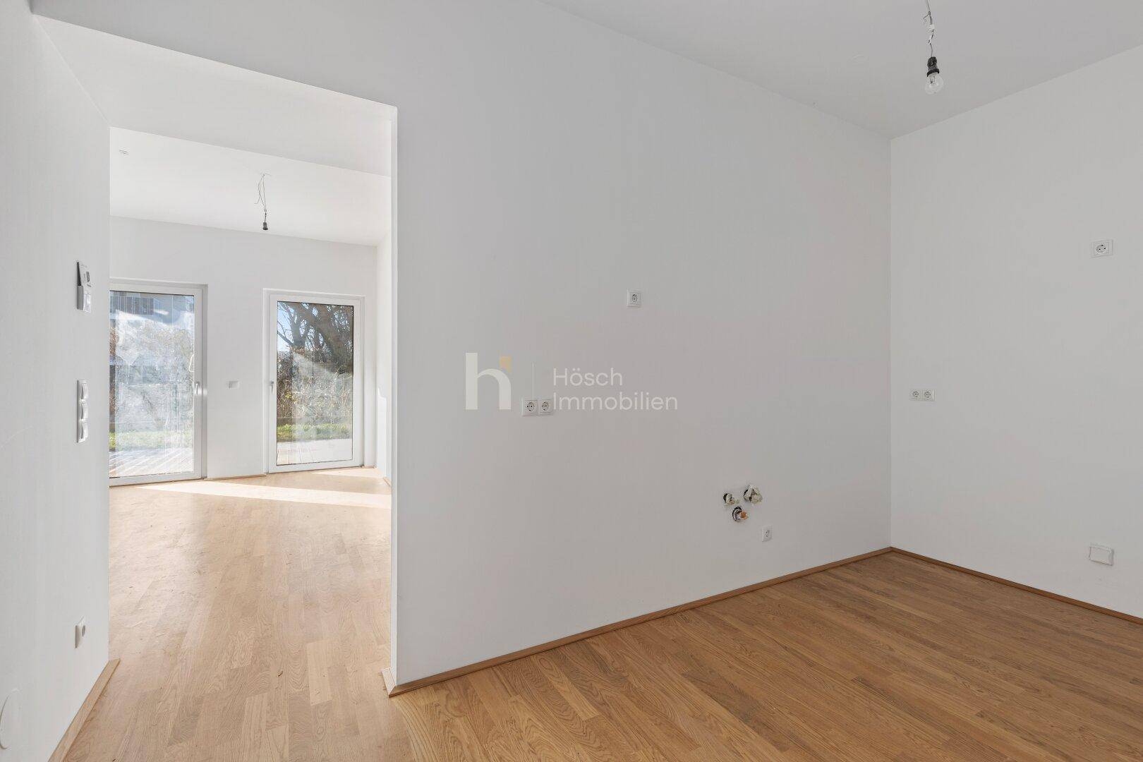 Leerer Raum mit Holzboden und Anschlüssen für eine Küche, bereit für den Einbau.