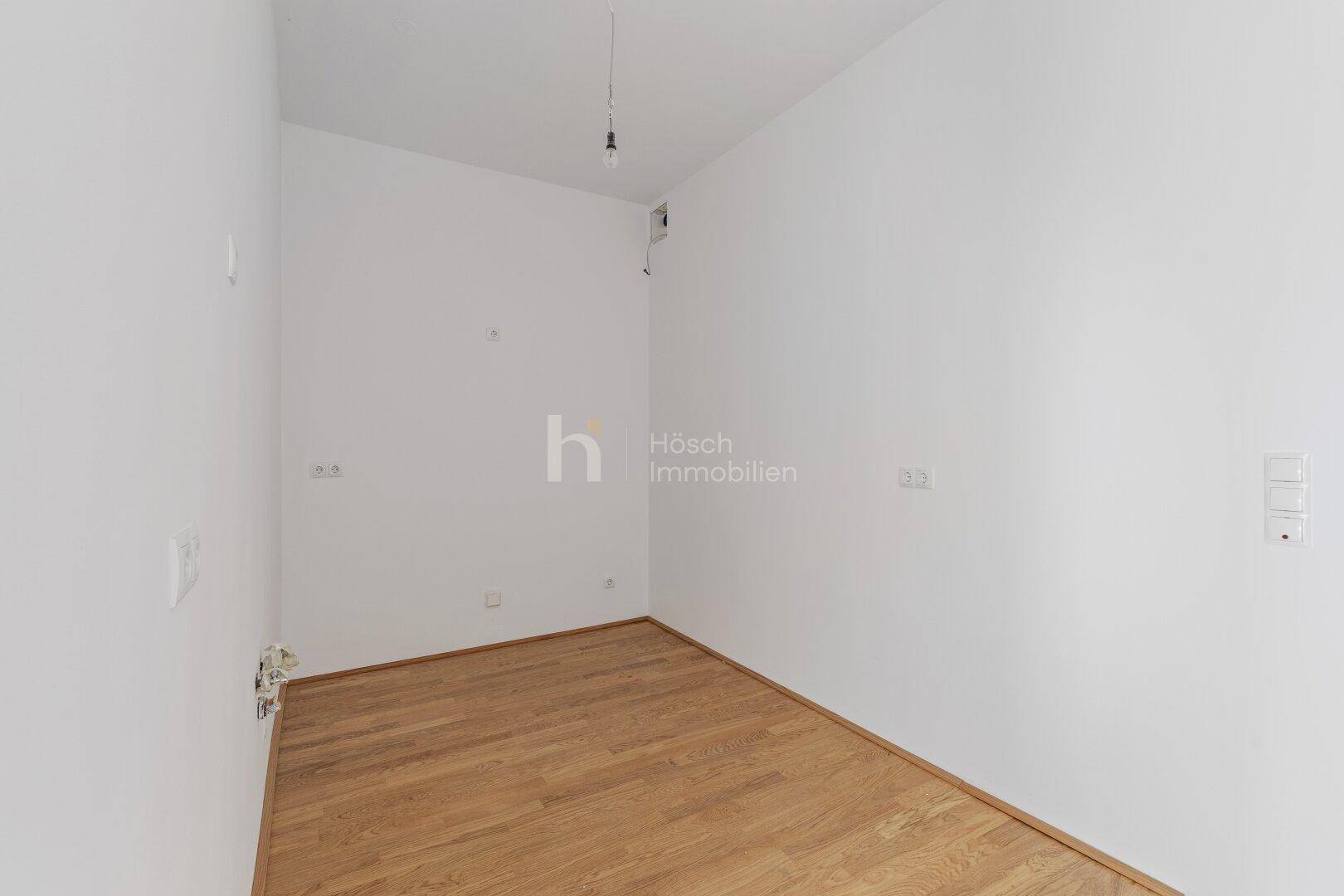Heller Raum mit Holzboden und vorbereiteten Anschlüssen für eine moderne Einbauküche.