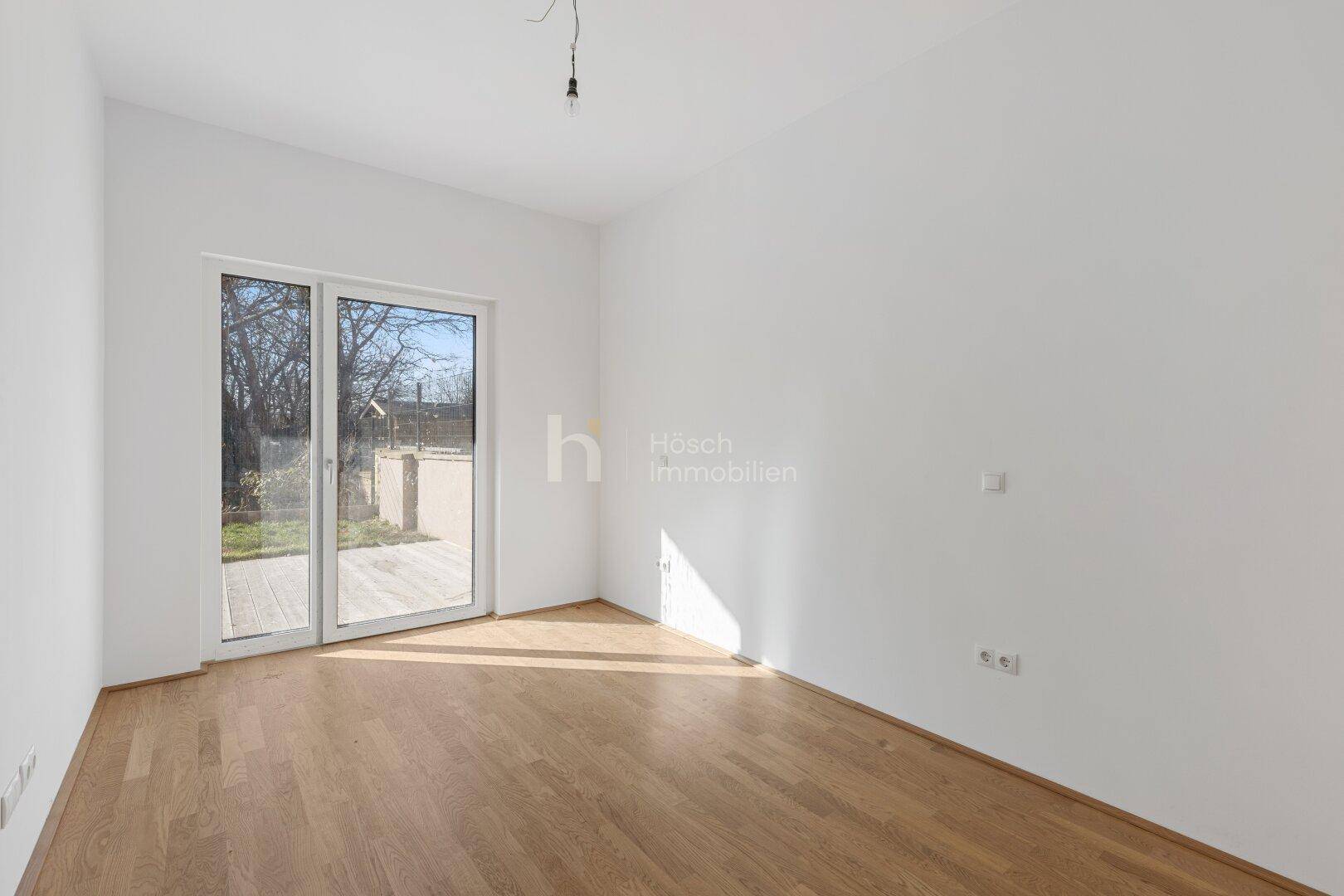 Sonniger Raum mit Holzboden und einer breiten Glastür, die viel Tageslicht hereinlässt.