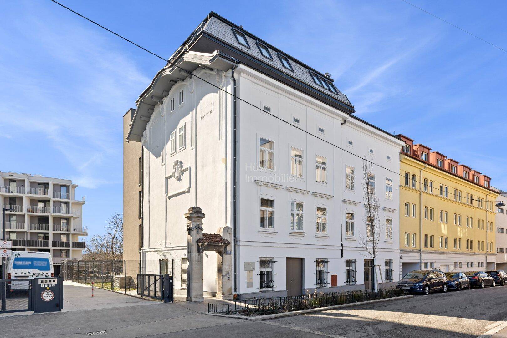 Weißes historisches Gebäude mit Mansarddach und klassischer Architektur in einer belebten Stadtstraße.