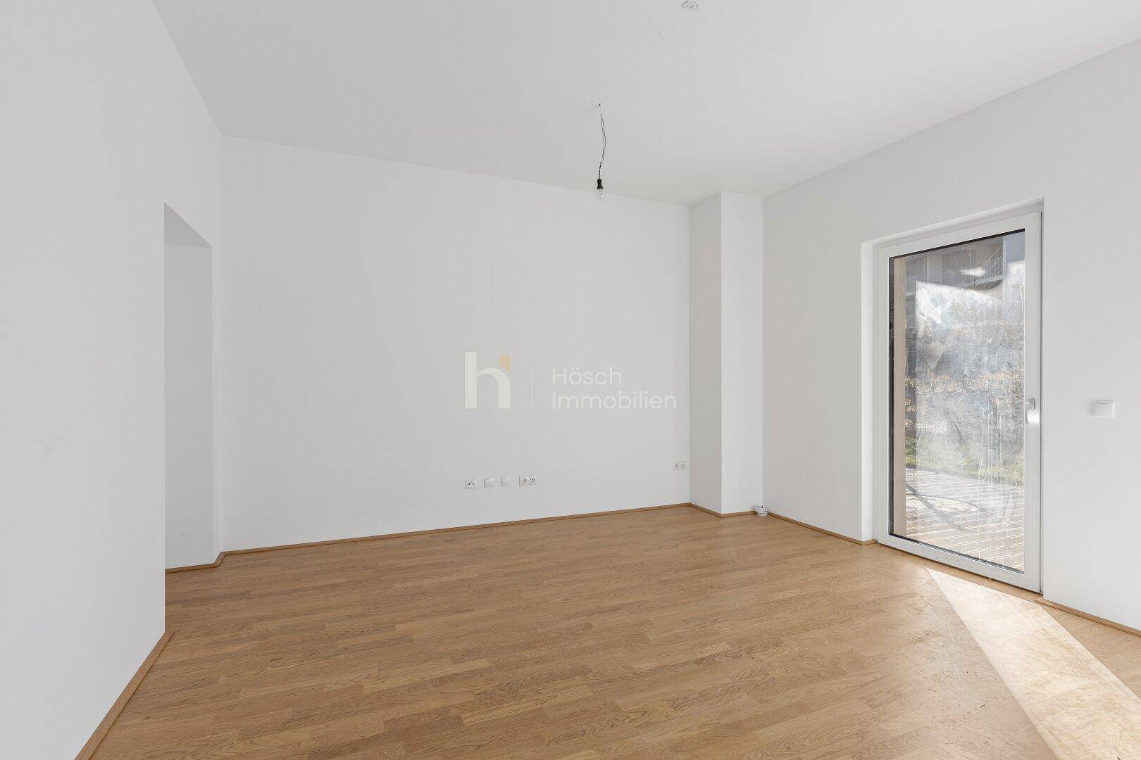 Lichtdurchfluteter Raum mit hellem Holzboden und einer großen Glastür zum Außenbereich.