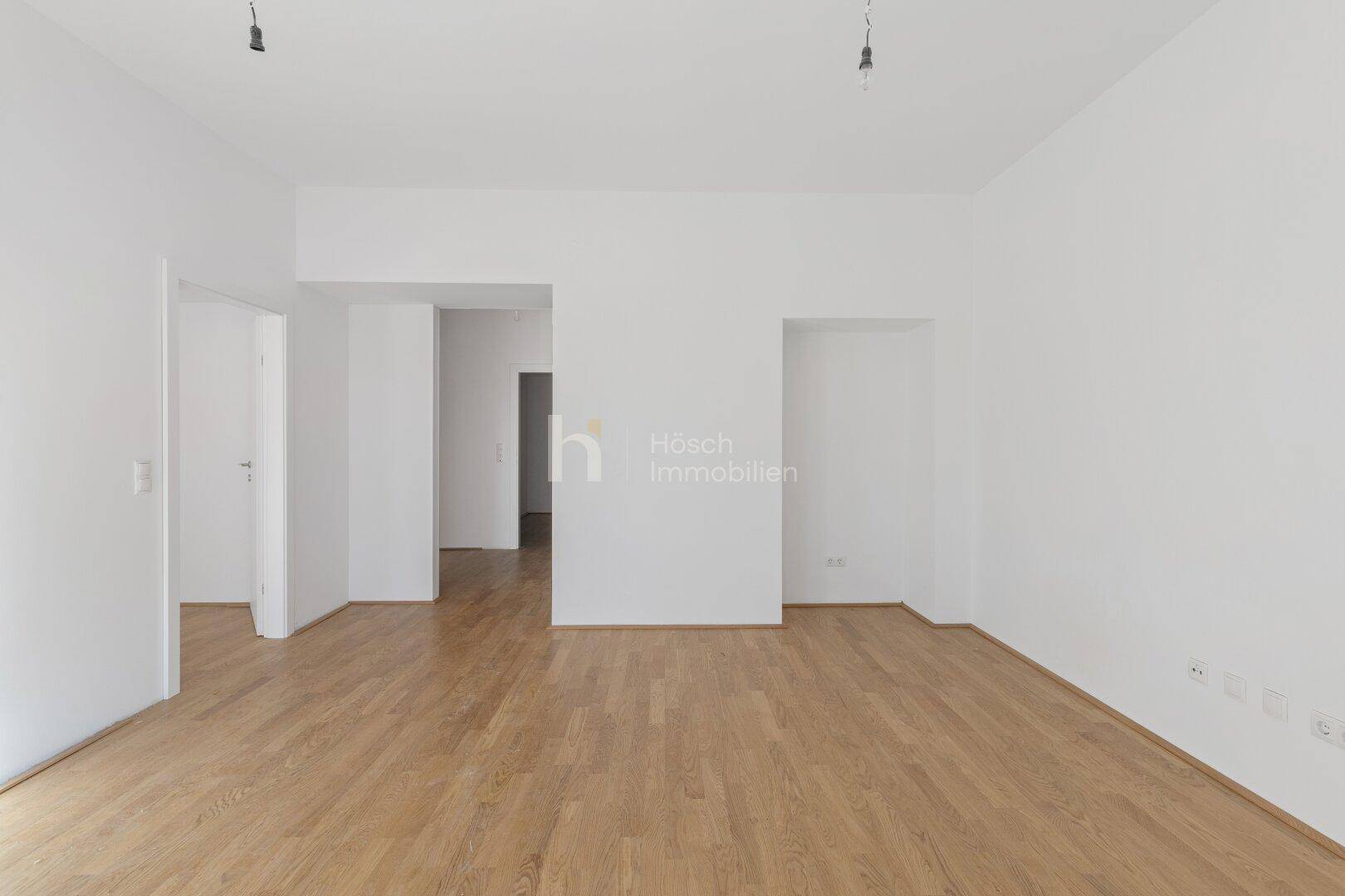 Geräumiger, heller Raum mit Holzboden und offenen Durchgängen zu weiteren Bereichen der Wohnung.