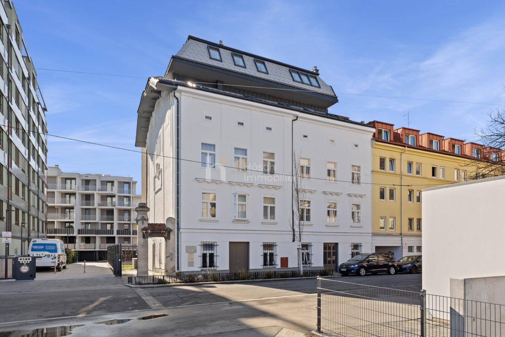 Historisches Gebäude mit moderner Dachaufstockung und Mansarddach in urbaner Umgebung.