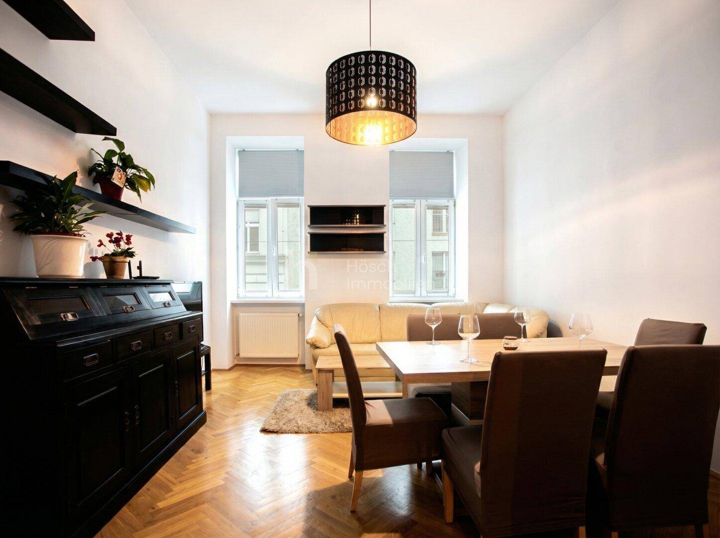 Gemütlicher Wohn- und Essbereich mit Holztisch, beigem Sofa und Fischgrätparkett.