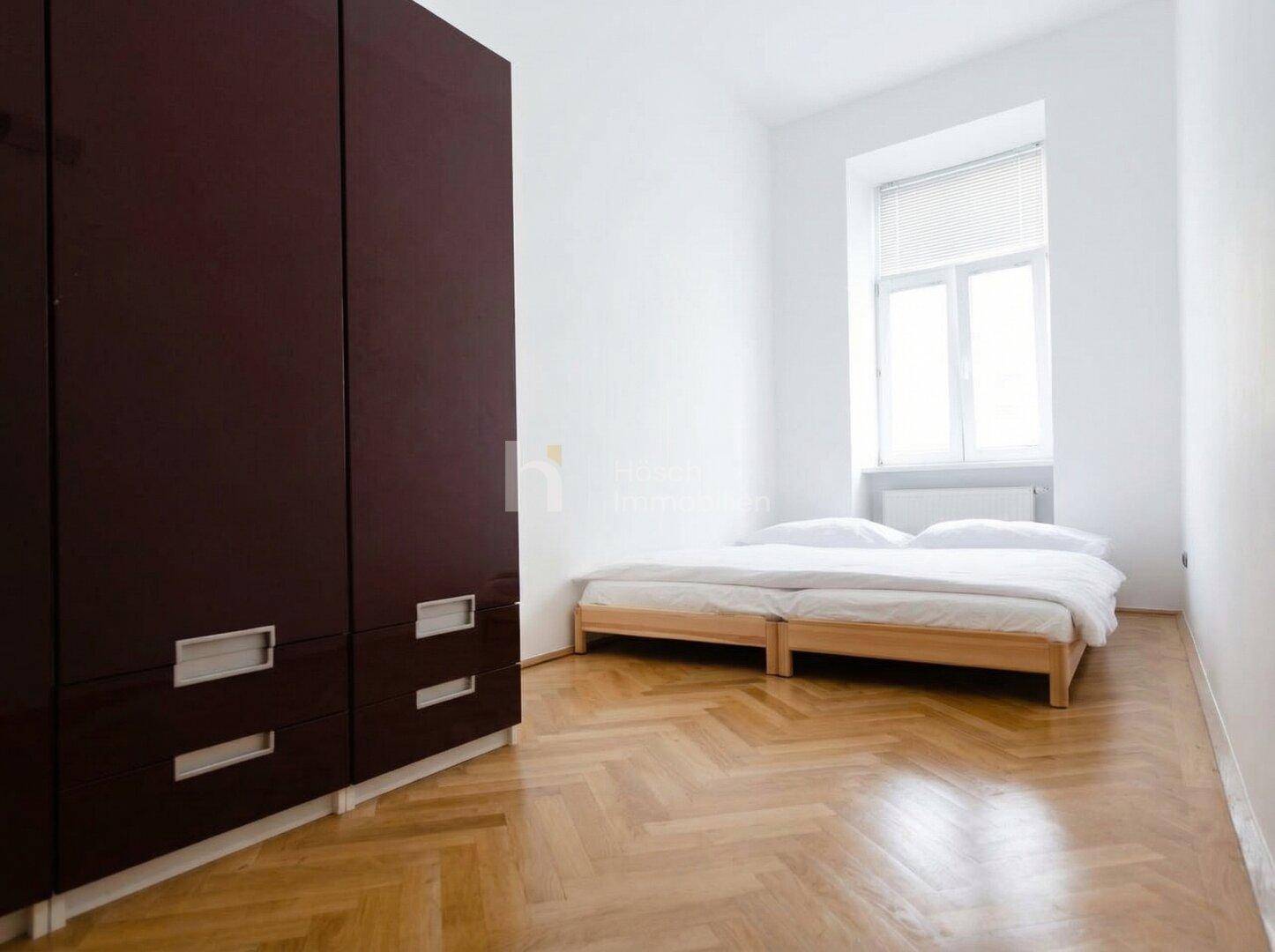 Schlafzimmer mit großem Kleiderschrank, Holzbett und Fischgrätparkett.