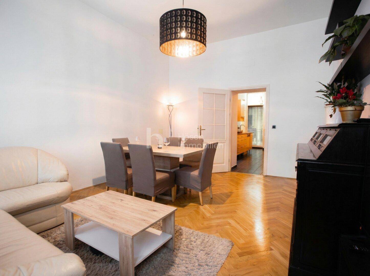 Wohn- und Essbereich mit Holztisch, beigem Sofa und Zugang zu einem weiteren Raum.