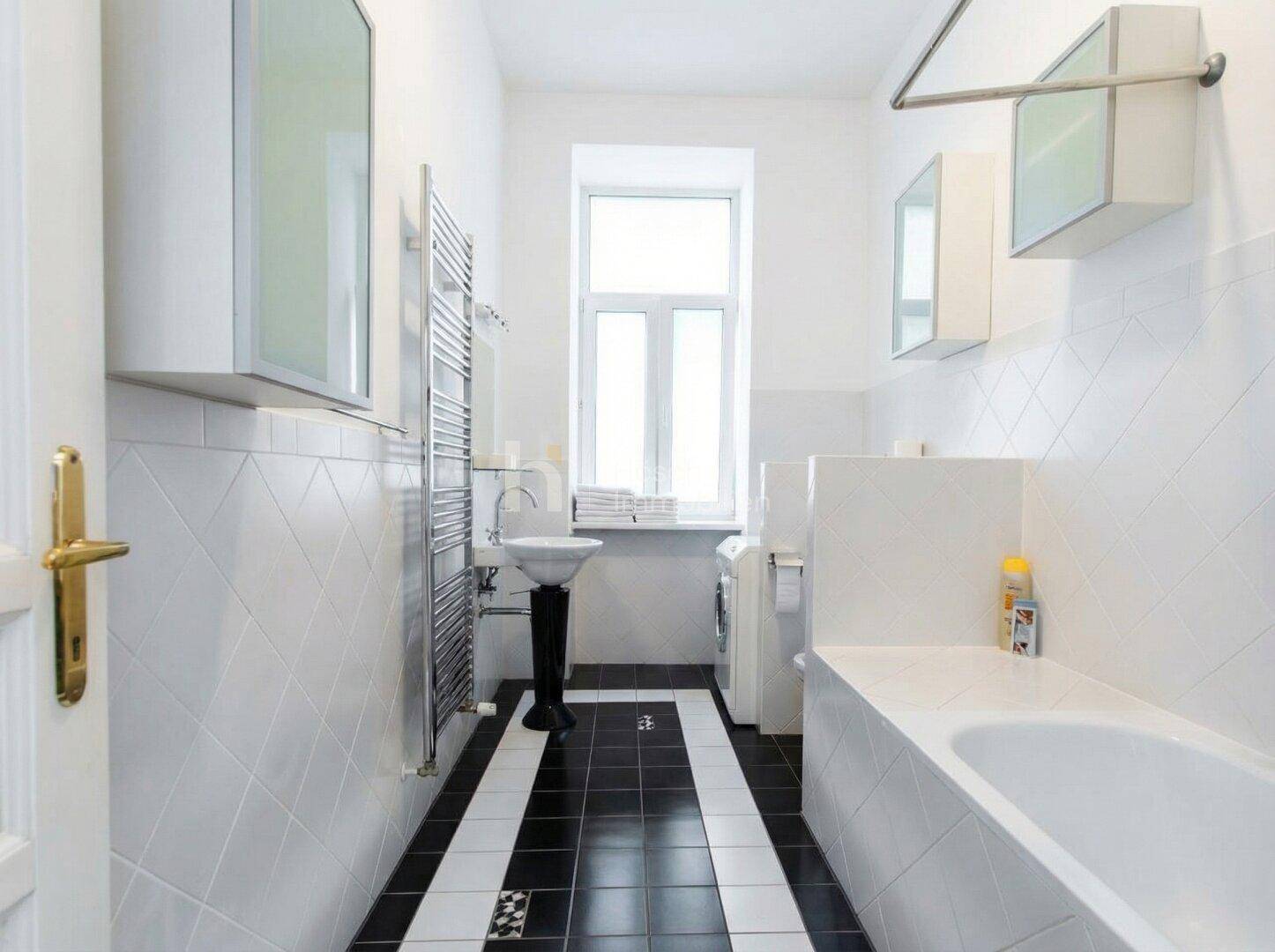 Modernes Badezimmer mit schwarz-weißen Fliesen, Badewanne, Fenster und Handtuchheizkörper.