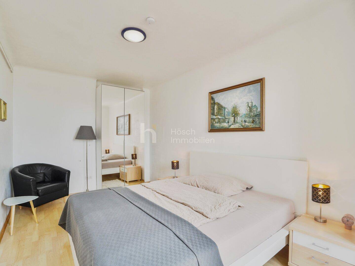 Schlafzimmer mit Doppelbett, Spiegelschrank und hellem Holzboden.