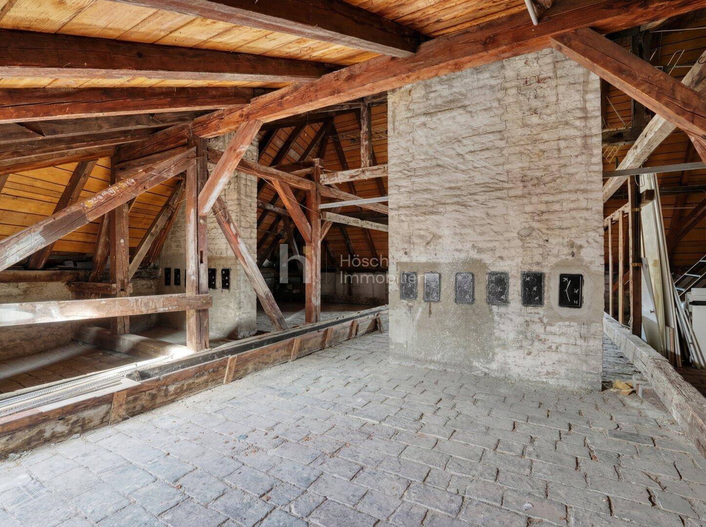 Unausgebauter Dachboden mit freiliegenden Holzbalken und gemauerten Schornsteinen, bietet viel Potenzial.