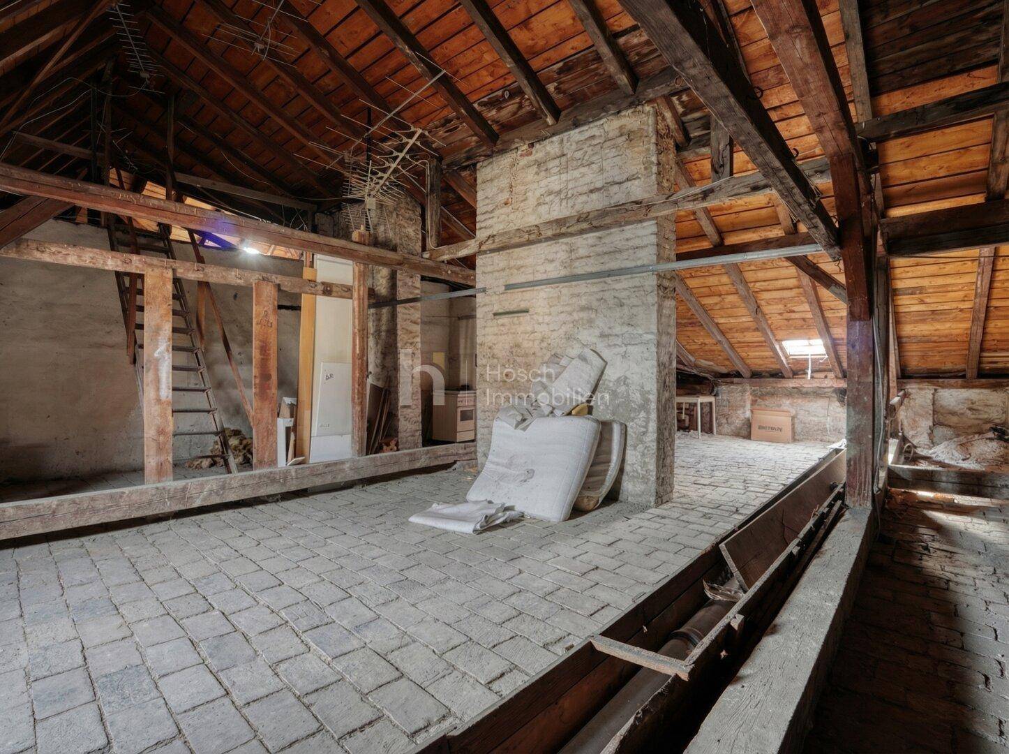 Unausgebauter Dachboden mit sichtbaren Holzbalken und Ziegelwänden, bietet Ausbaupotenzial.
