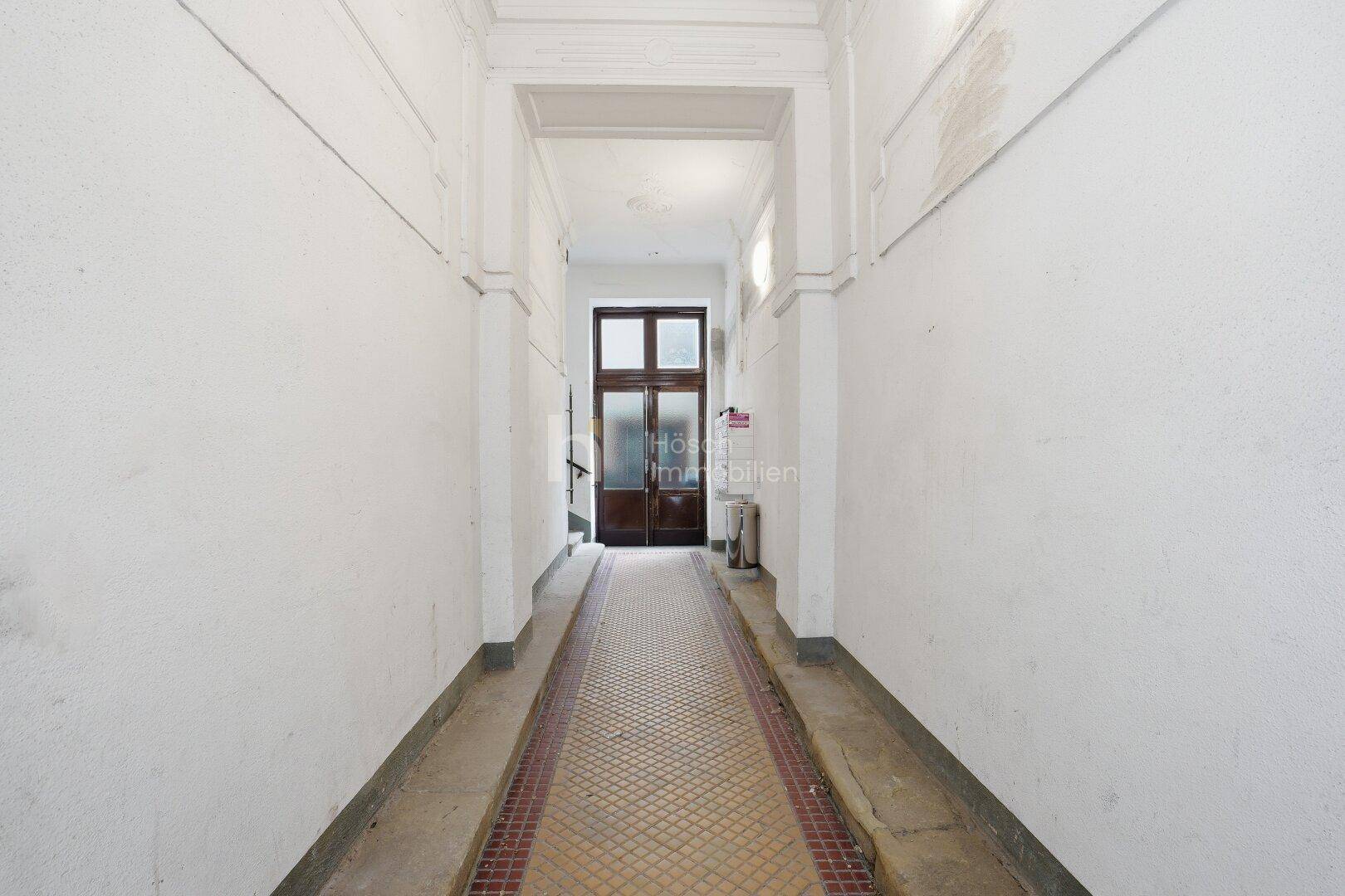 Historischer Eingangsbereich mit originalen Fliesen und hohen Decken, typisch für Altbau.