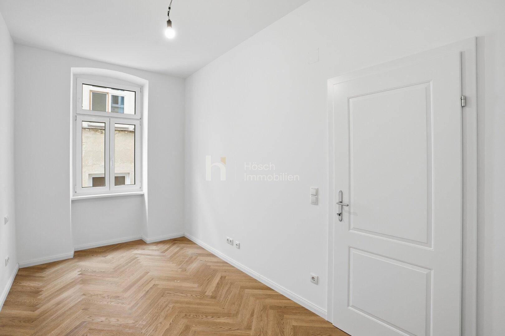 Renoviertes Zimmer mit Fischgrätparkett und weißer Tür, ideal für ein Kinder- oder Arbeitszimmer.