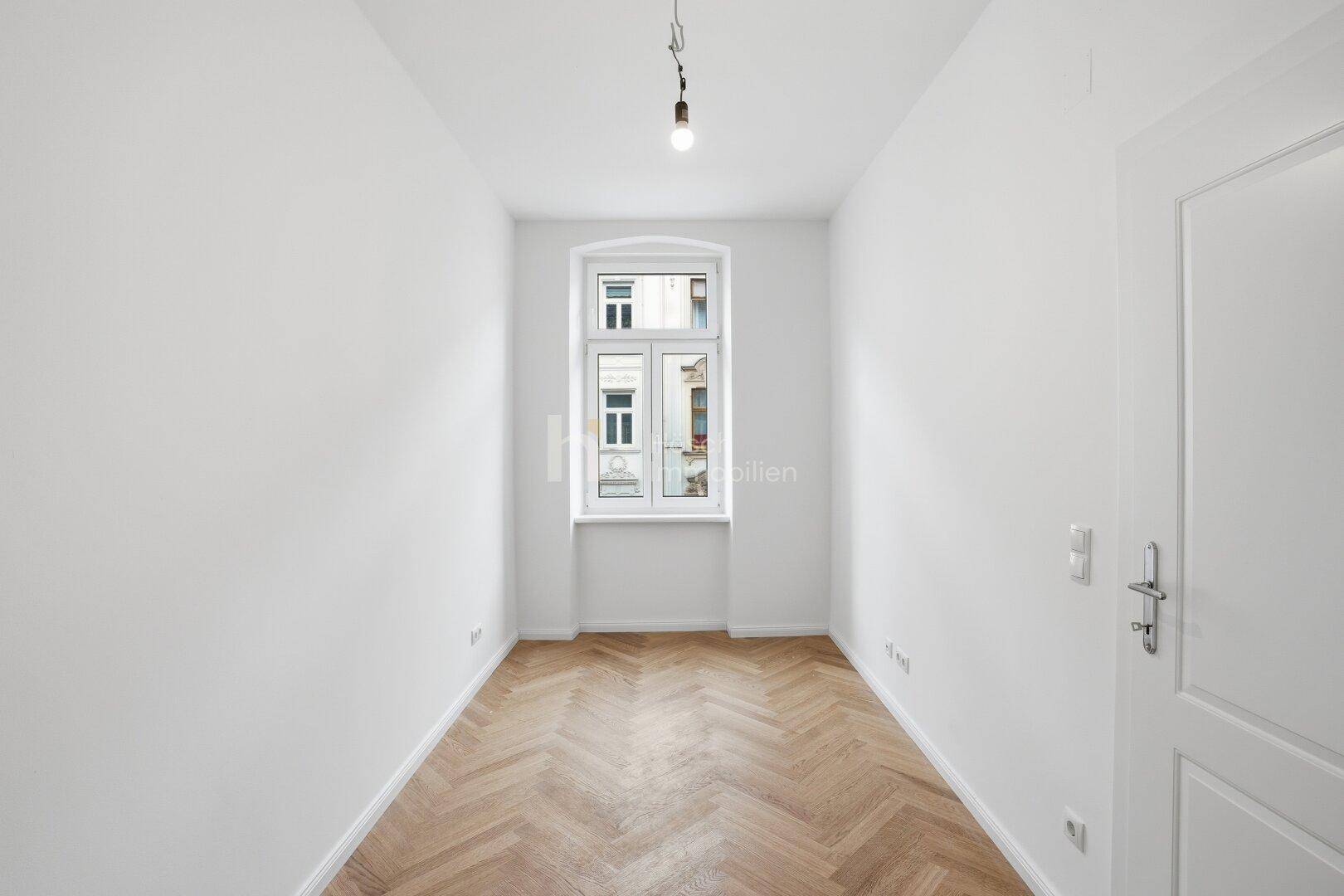 Lichtdurchflutetes Zimmer mit Fischgrätparkett und einem großen Fenster, frisch renoviert.