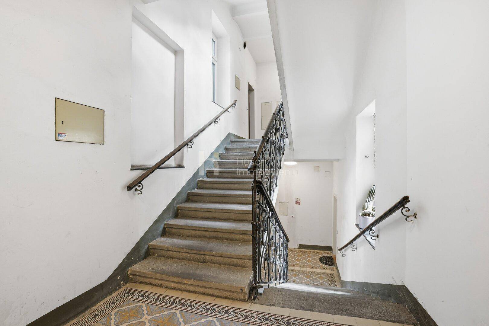Repräsentatives Treppenhaus eines Altbaus mit Steinstufen und kunstvollem Geländer.