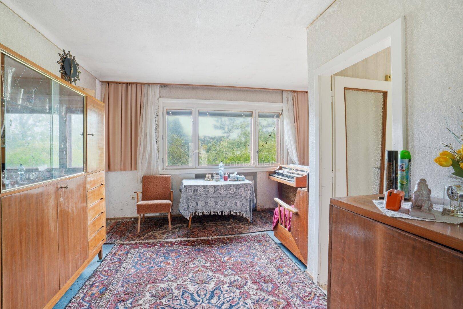 Zimmer mit großem Holzschrank, Esstisch und Fenster, das viel Tageslicht hereinlässt.