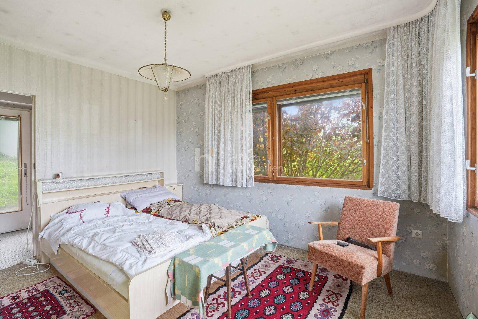 Schlafzimmer mit zwei Einzelbetten, gemusterter Tapete und großem Fenster mit Blick ins Grüne.