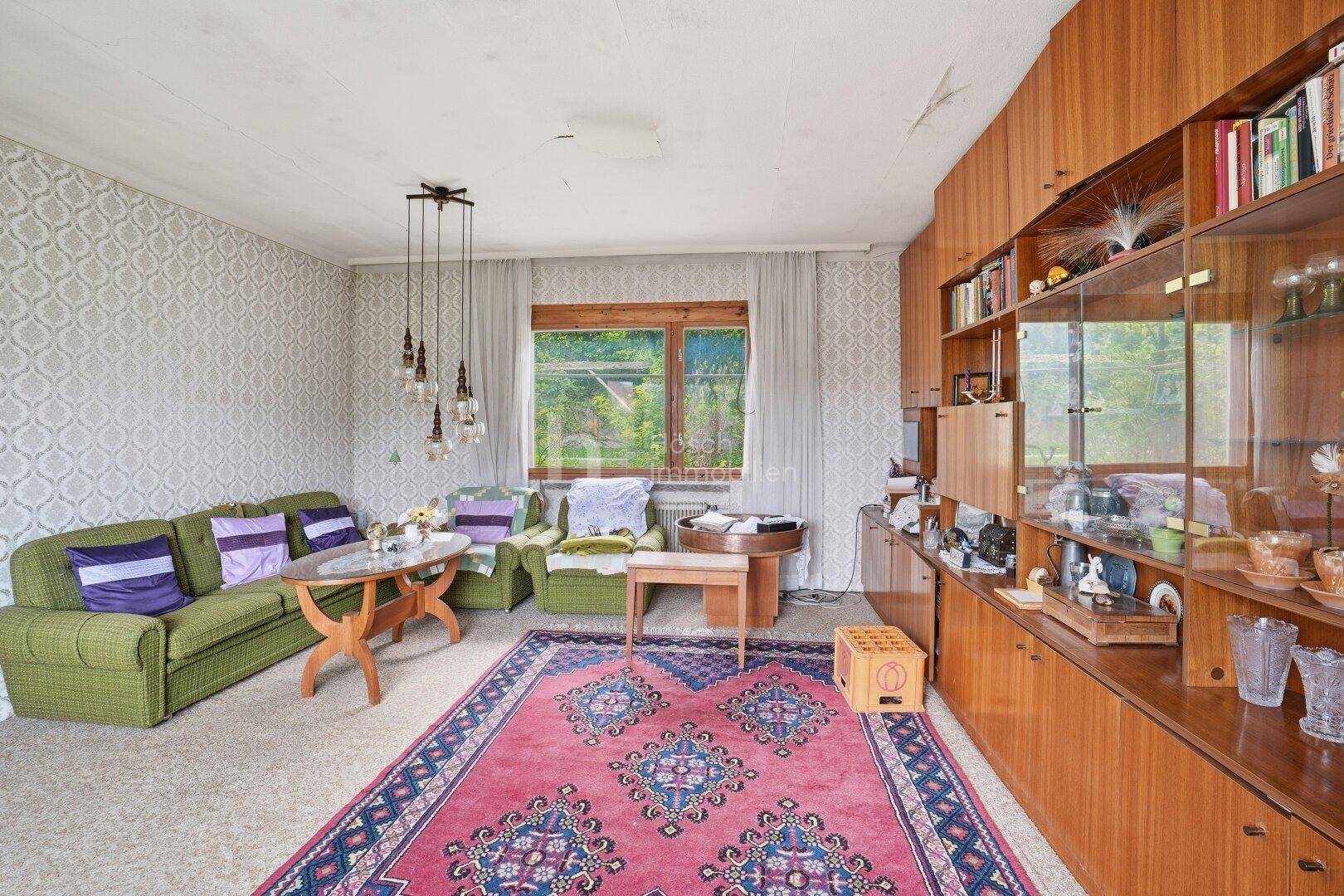 Wohnzimmer mit traditioneller Einrichtung, Holzmöbeln und einem großen Fenster mit Blick ins Grüne.