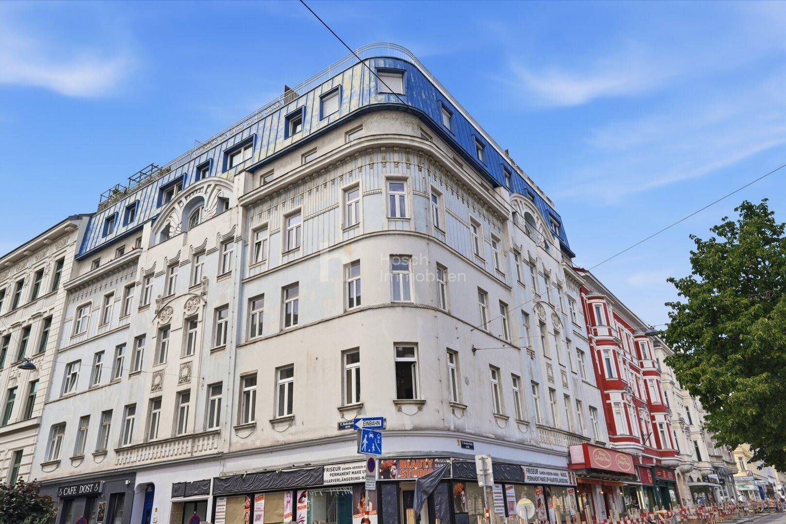 Historisches Eckgebäude mit einer markanten blauen Dachkonstruktion und Geschäften im Erdgeschoss in der Stadt.