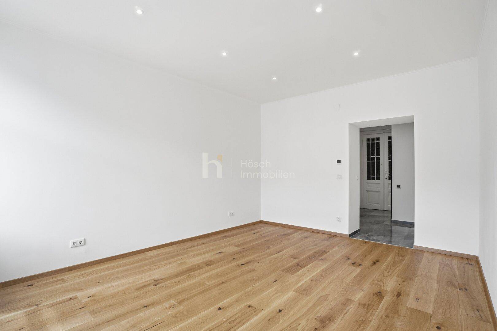 Leerer Raum mit Holzboden und Zugang zu einem gefliesten Bereich, ideal für flexible Nutzung.