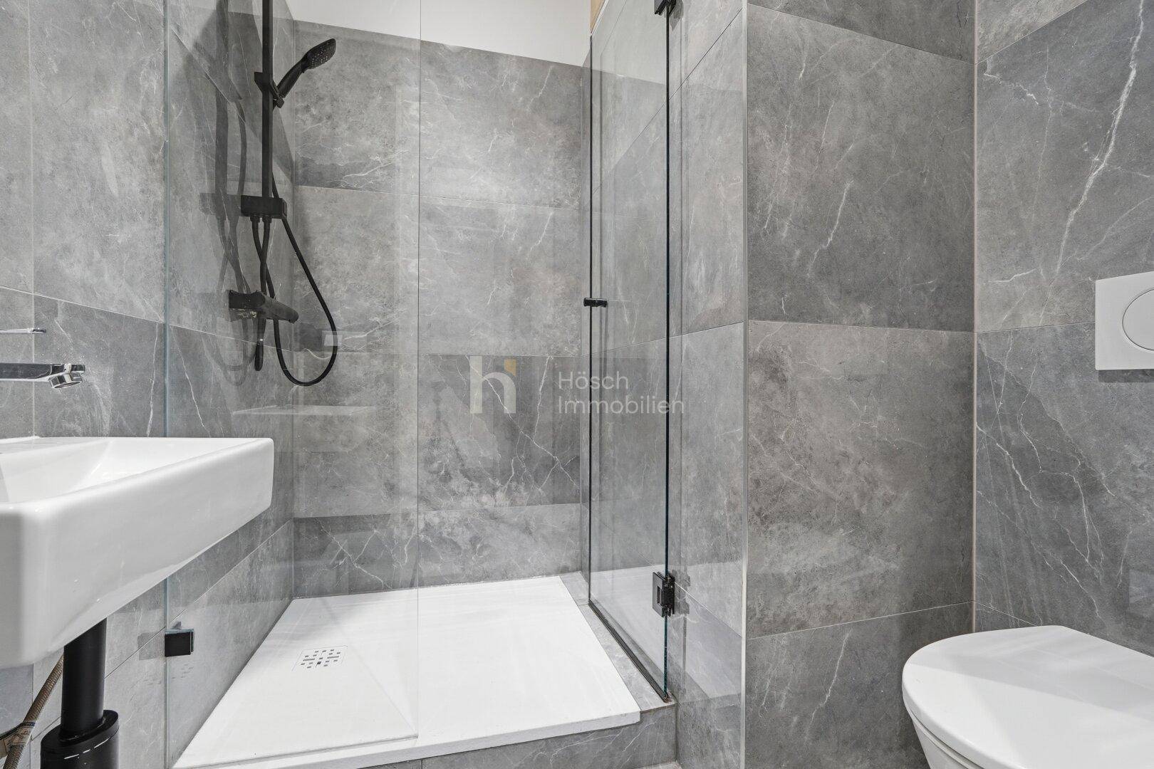 Helles Badezimmer mit moderner begehbarer Dusche, Waschbecken und wandhängendem WC, alles in Grau gehalten.