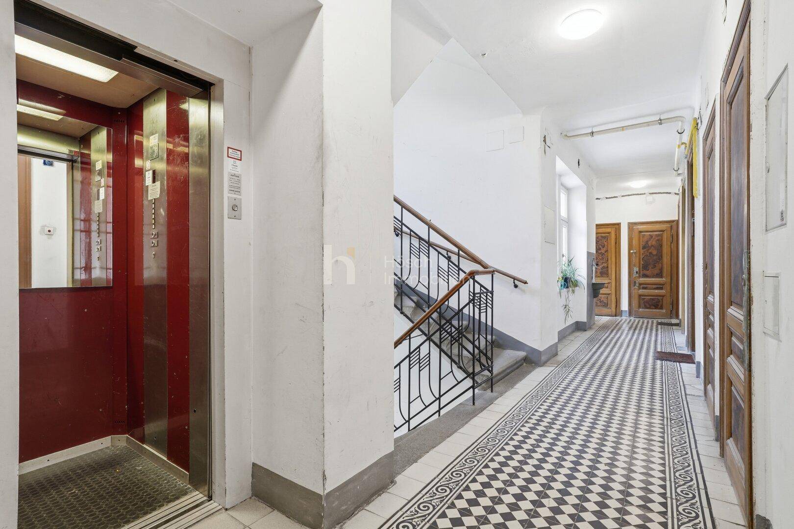 Eingangsbereich eines Altbaus mit Aufzug, Treppenhaus und einem gemusterten Fliesenboden.