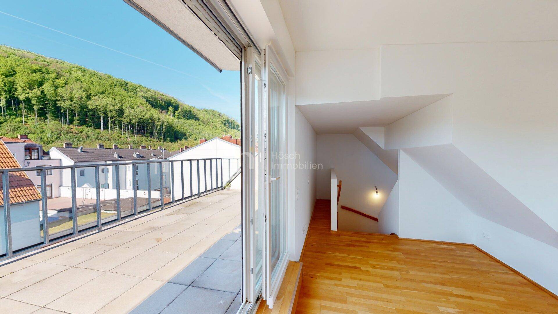 Heller Innenraum mit Holzfußboden, Treppenzugang und großer Glasschiebetür zur Terrasse mit Bergblick.