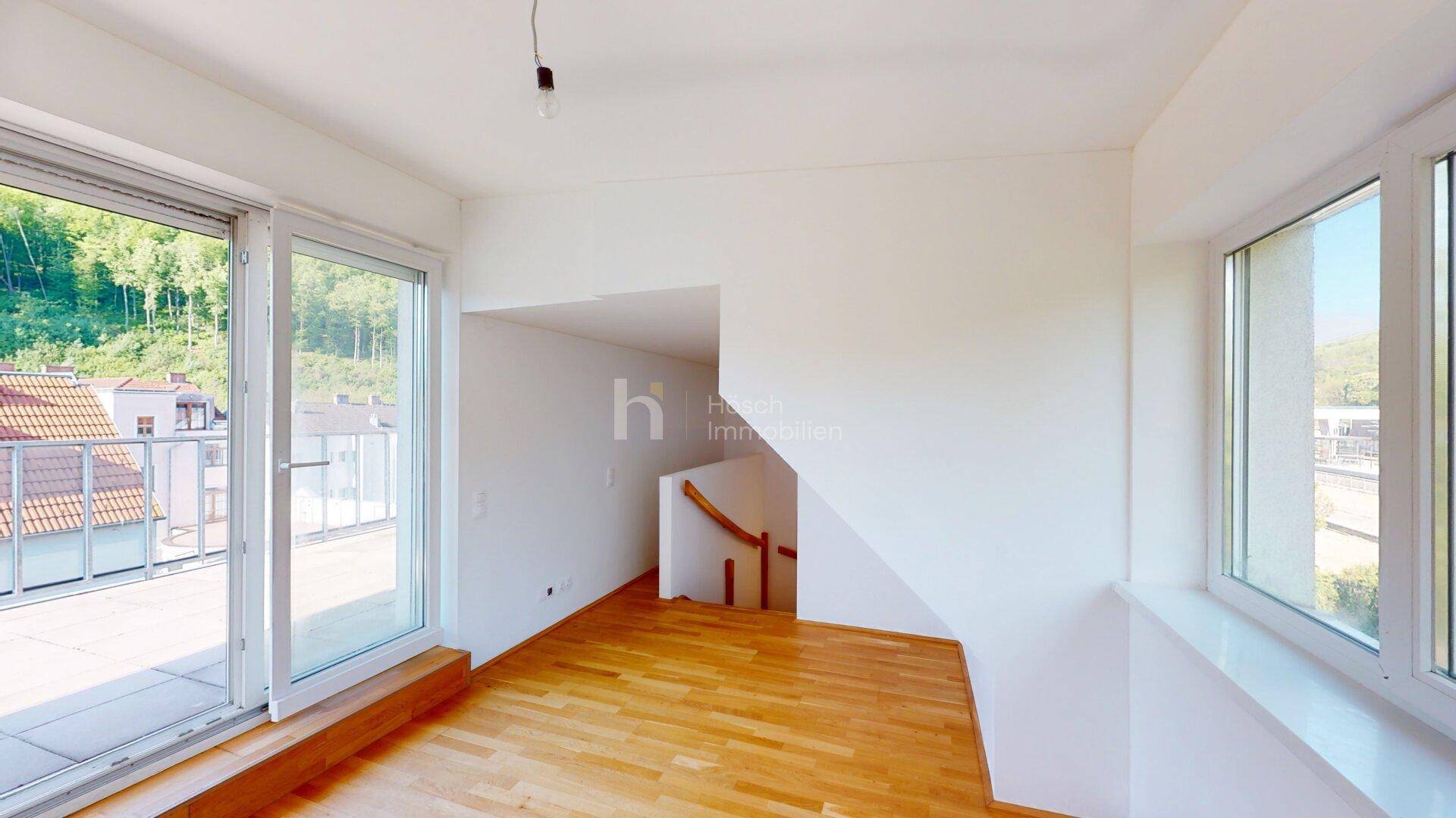 Heller Raum mit Holzboden, Zugang zur Terrasse und Blick auf die umliegende grüne Landschaft.