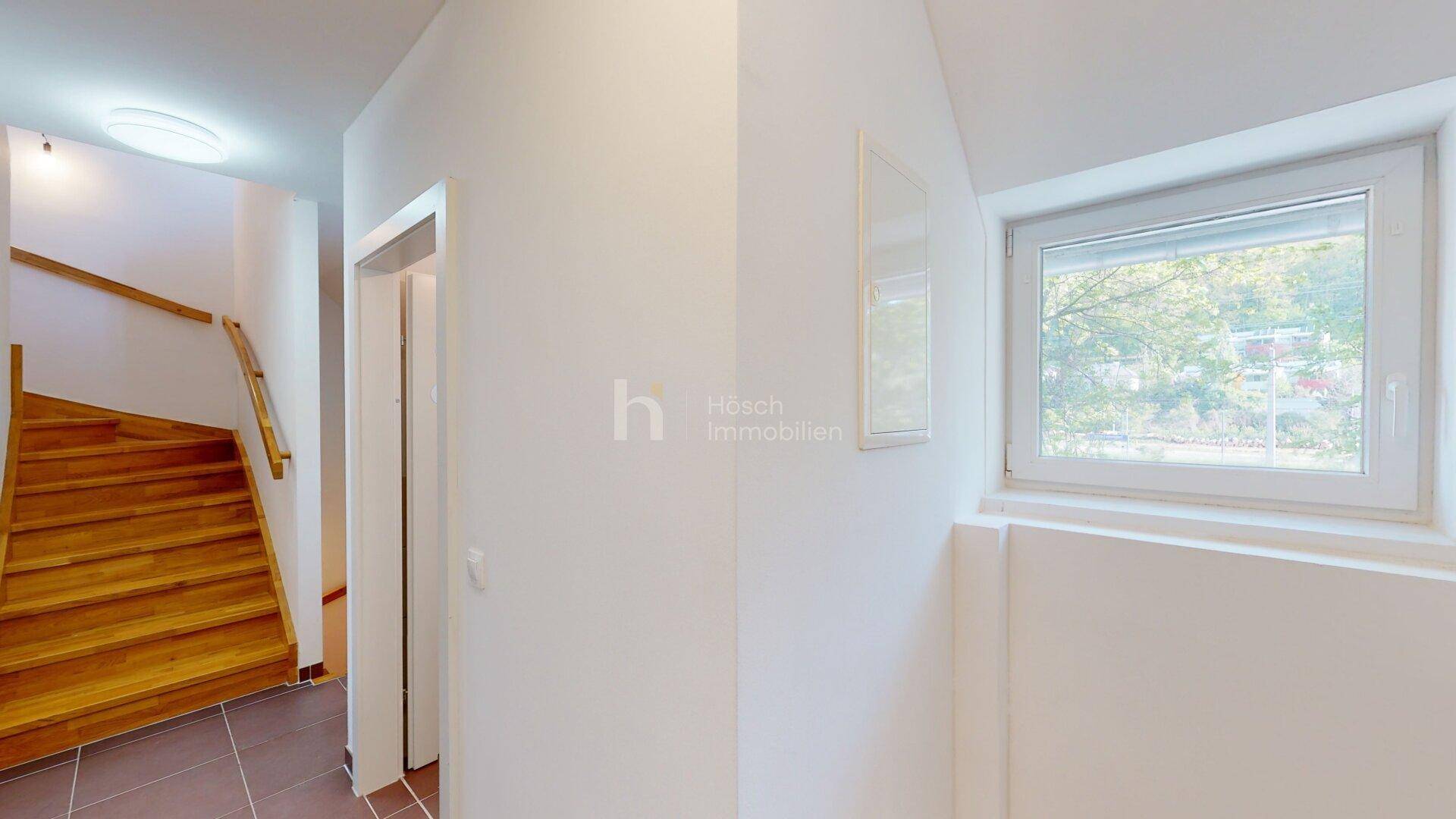 Heller Flur mit Holztreppe, Fliesenboden und einem Fenster für natürliches Licht.