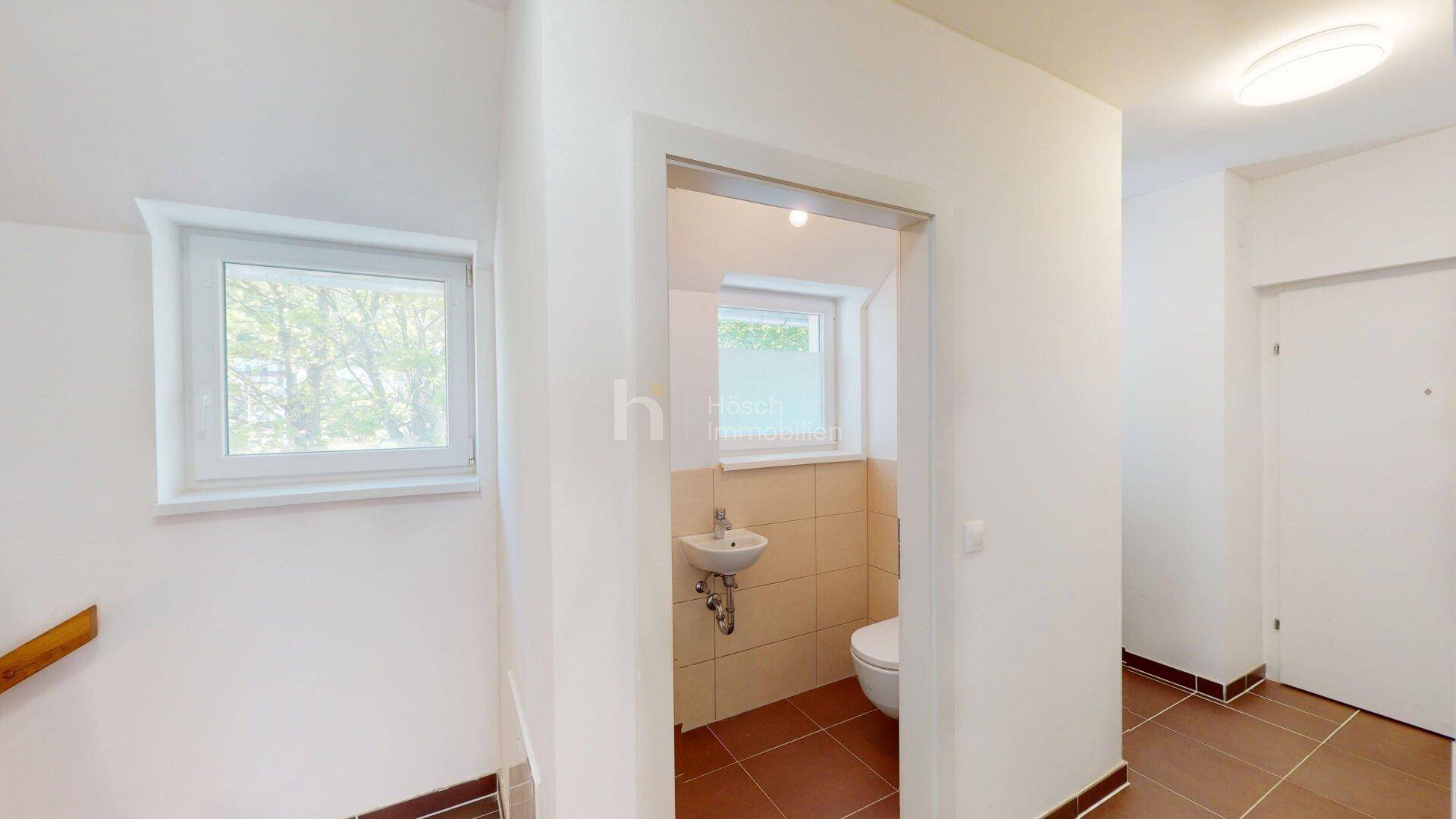 Flur mit Zugang zu einem hellen Gäste-WC, ausgestattet mit Fenster und kleinem Waschbecken.