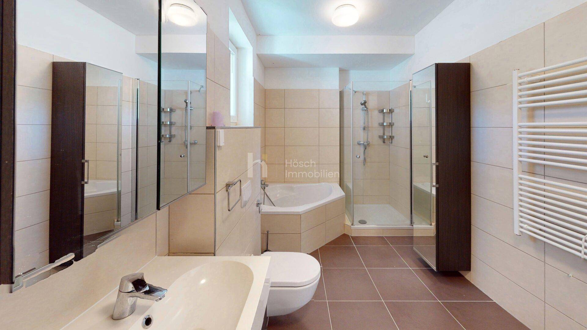Modernes Badezimmer mit beigen Fliesen, Eckbadewanne, Duschkabine und beheiztem Handtuchhalter.